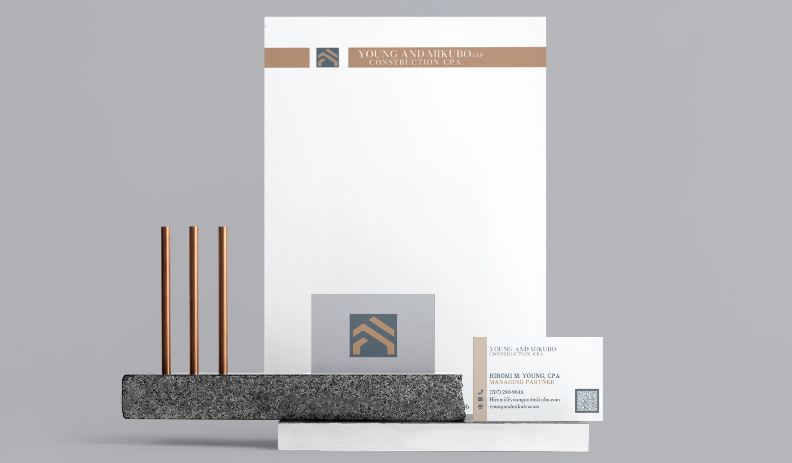 Branding materials for Young and Mikubo LLP Construction CPA, including a letterhead, business card, and logo, displayed on stacked rectangular bases with three vertical rods to showcase their Texas CPA stationery design.