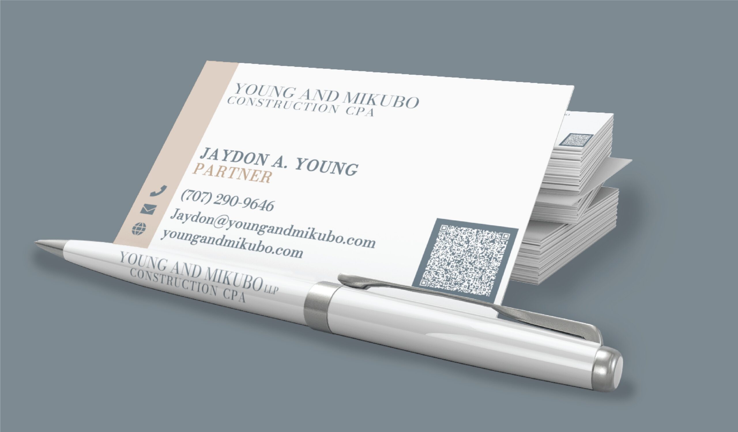 A stack of Young and Mikubo Construction CPA business cards with contact details and a QR code, displayed with a branded pen as part of a professional stationery design.