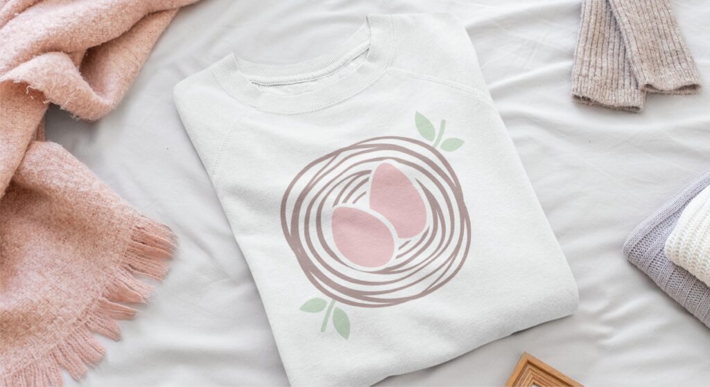 White sweatshirt with a graphic of two pink eggs in a brown nest with light green leaves, designed for Florida mental health services branding.