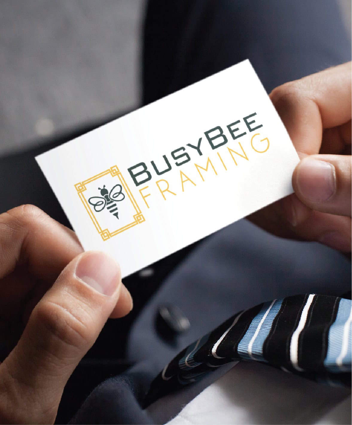 A person holds a business card for BusyBee Framing, displaying a professional logo design of a bee inside a geometric frame.