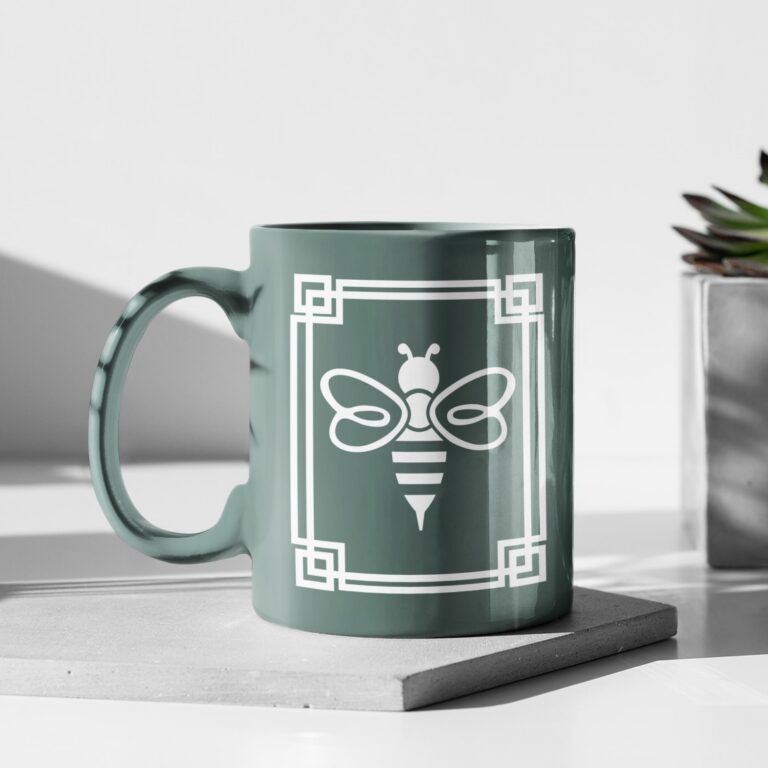 A sage green mug featuring a professional logo design of a bee centered within a white, square geometric border.