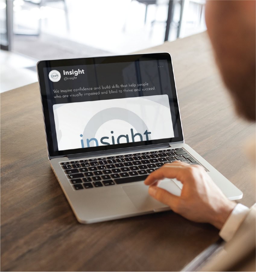 A person uses a laptop displaying an Insight social media design profile with a mission statement about supporting visually impaired and blind people.