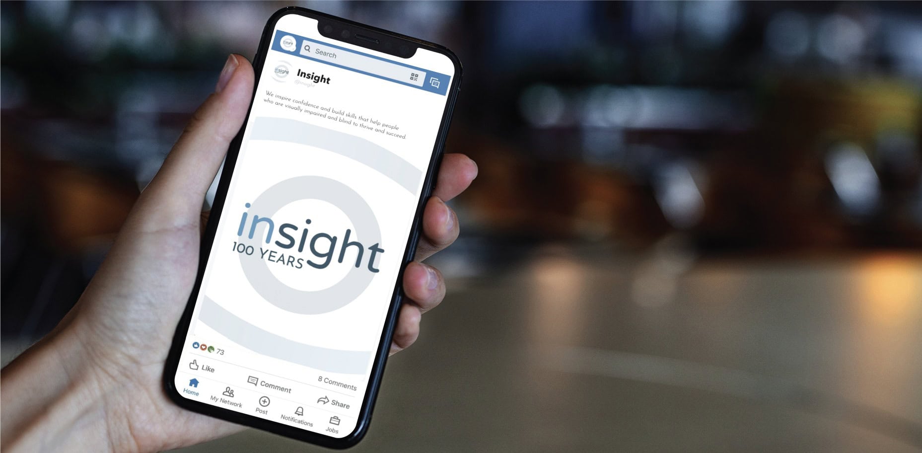 A hand holds a smartphone displaying a social media design for the Insight nonprofit, featuring a post that reads insight 100 YEARS.