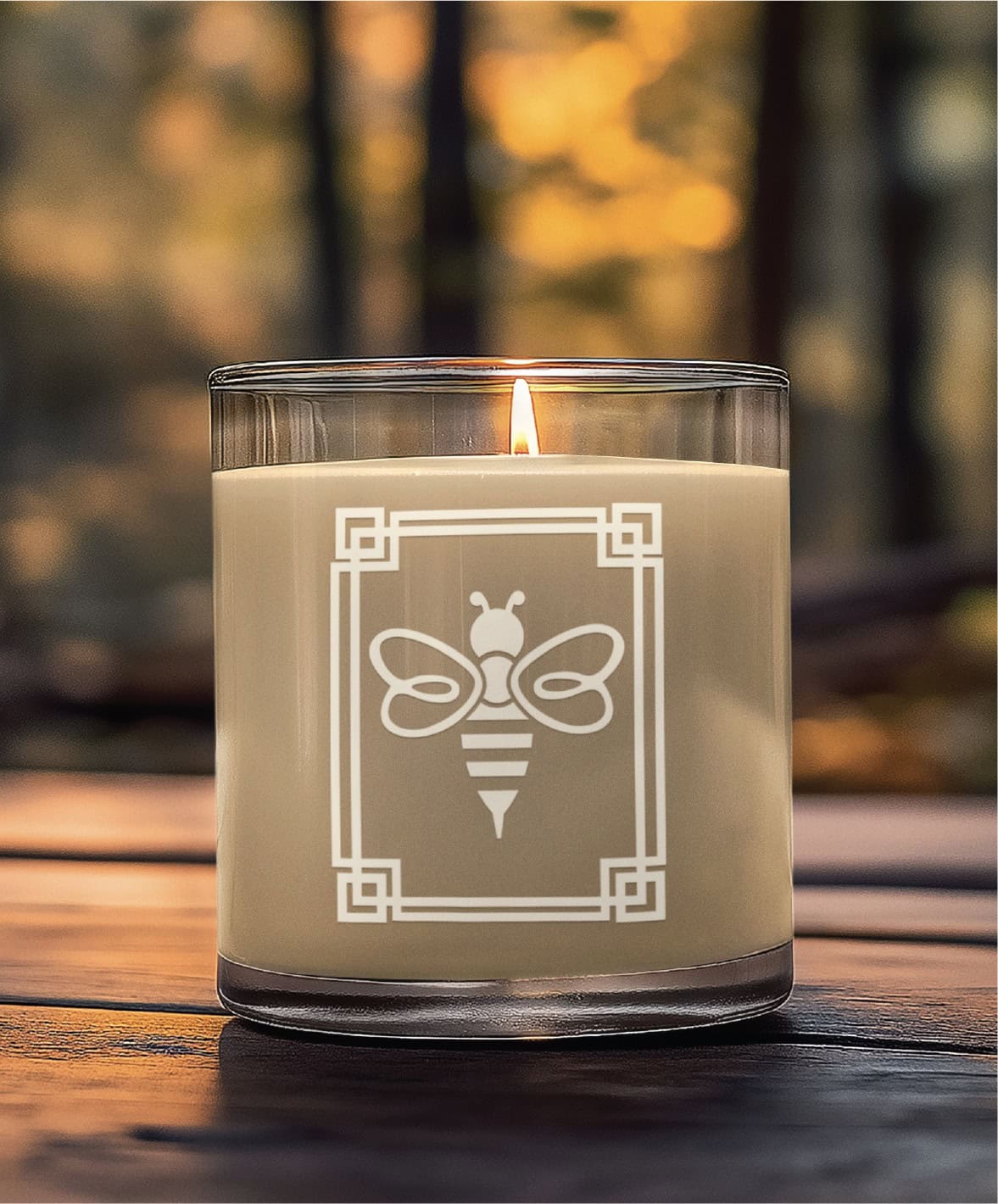 A lit candle in a glass jar featuring a white bee graphic inside a rectangular art frame.