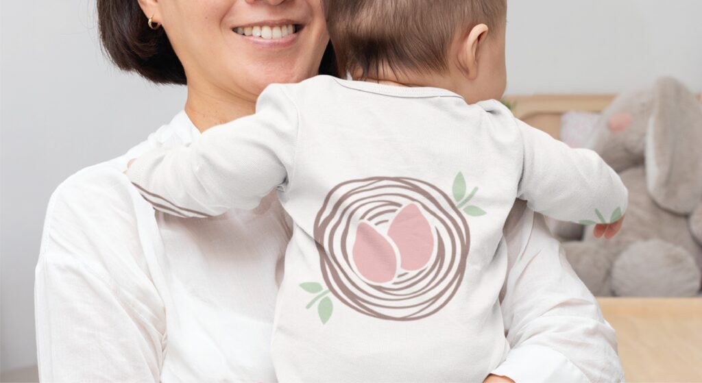 A Florida sleep consultant holds a baby wearing a white long-sleeved onesie decorated with a graphic of two eggs in a nest.