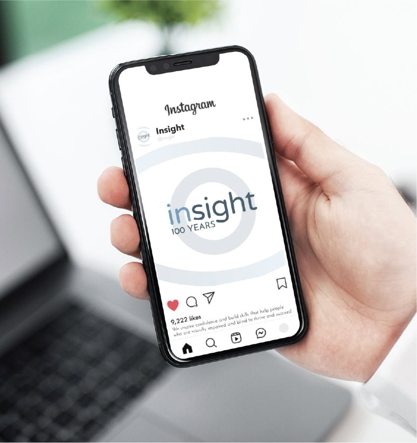 A hand holds a smartphone displaying an Instagram post by Insight, featuring a logo that reads Insight 100 YEARS and a caption about nonprofit marketing for the visually impaired.