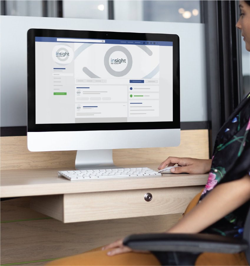 A person sits at a desk using a computer to view a social media design for the Rhode Island nonprofit Insight 100 Years.