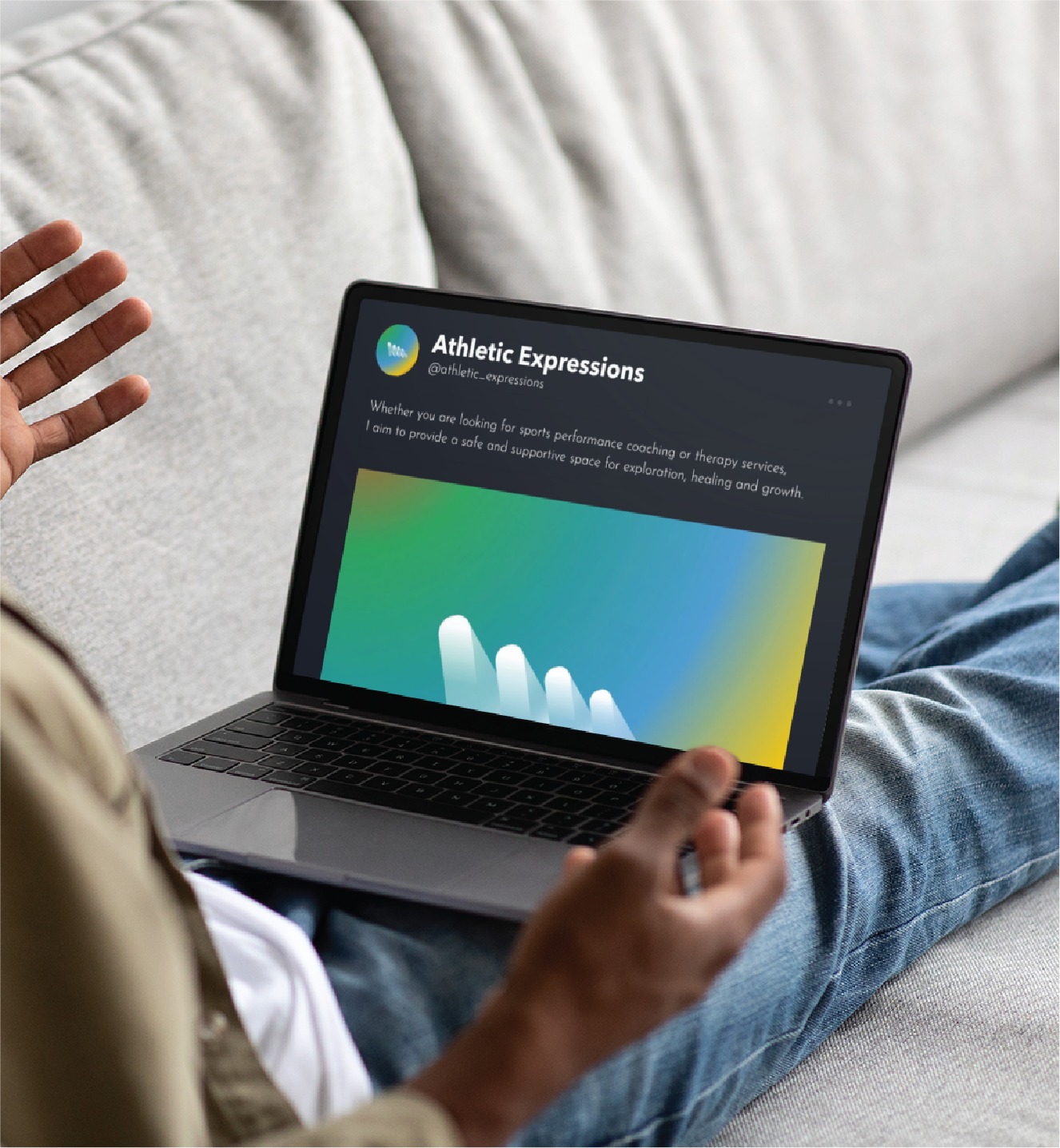 A person sits on a sofa viewing an Athletic Expressions social media design on a laptop screen.