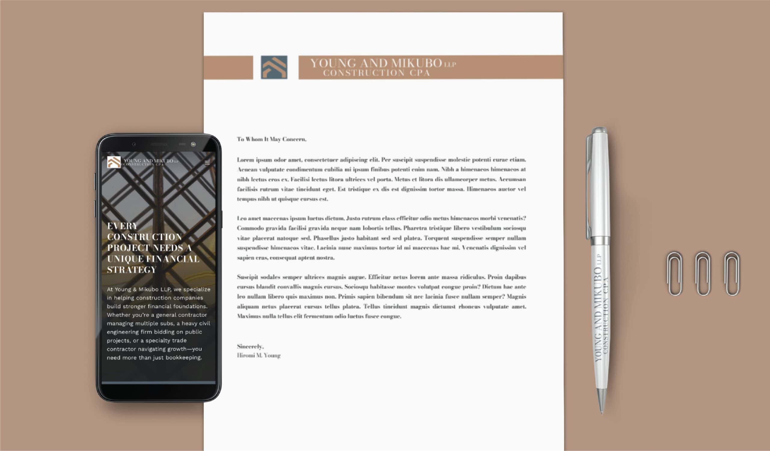 A construction CPA’s letterhead, a smartphone displaying a business website, and a branded pen on a desk with three paperclips.