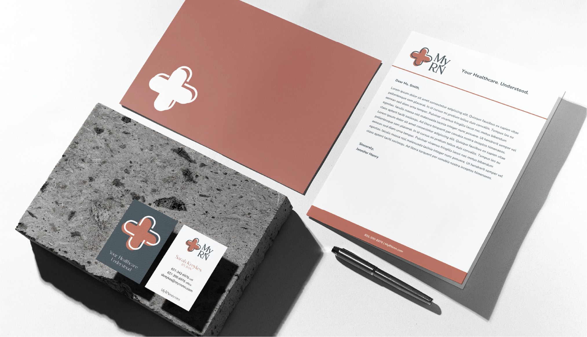 Custom stationery for My RN healthcare, including a letterhead, envelope, and business card with a plus sign logo, arranged on a textured stone surface with a pen.