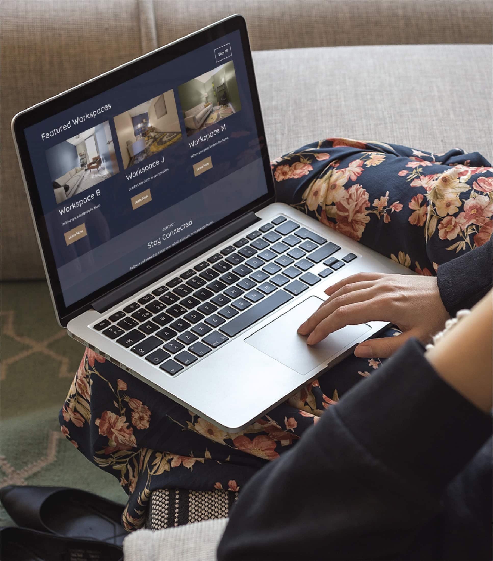 A person sits on a couch with a floral blanket, using a laptop to browse available workspaces and RN Services on a Minnesota website.