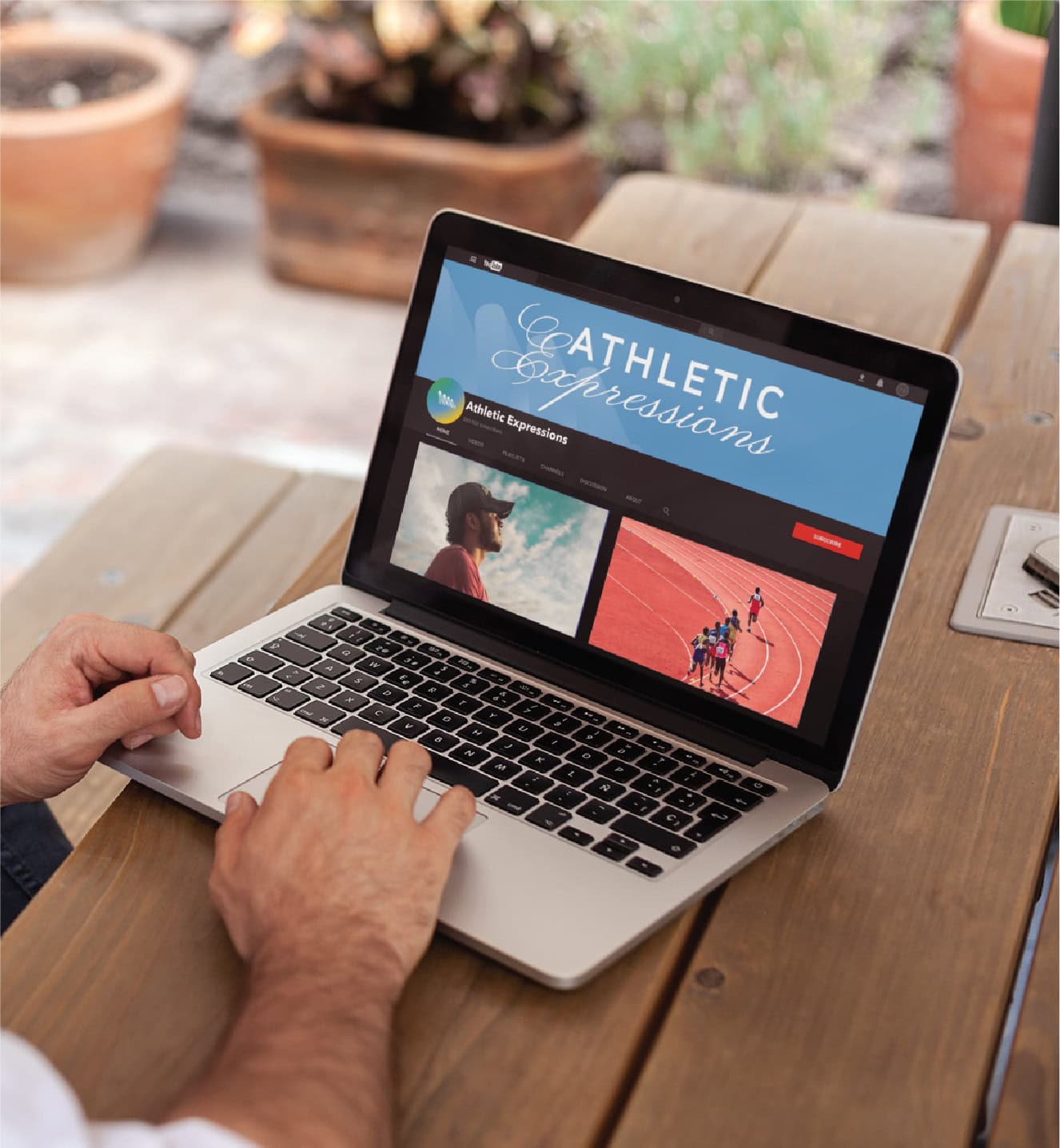 A person using a laptop on a wooden table to view the Athletic Expressions YouTube channel, showcasing California sports performance coaching.