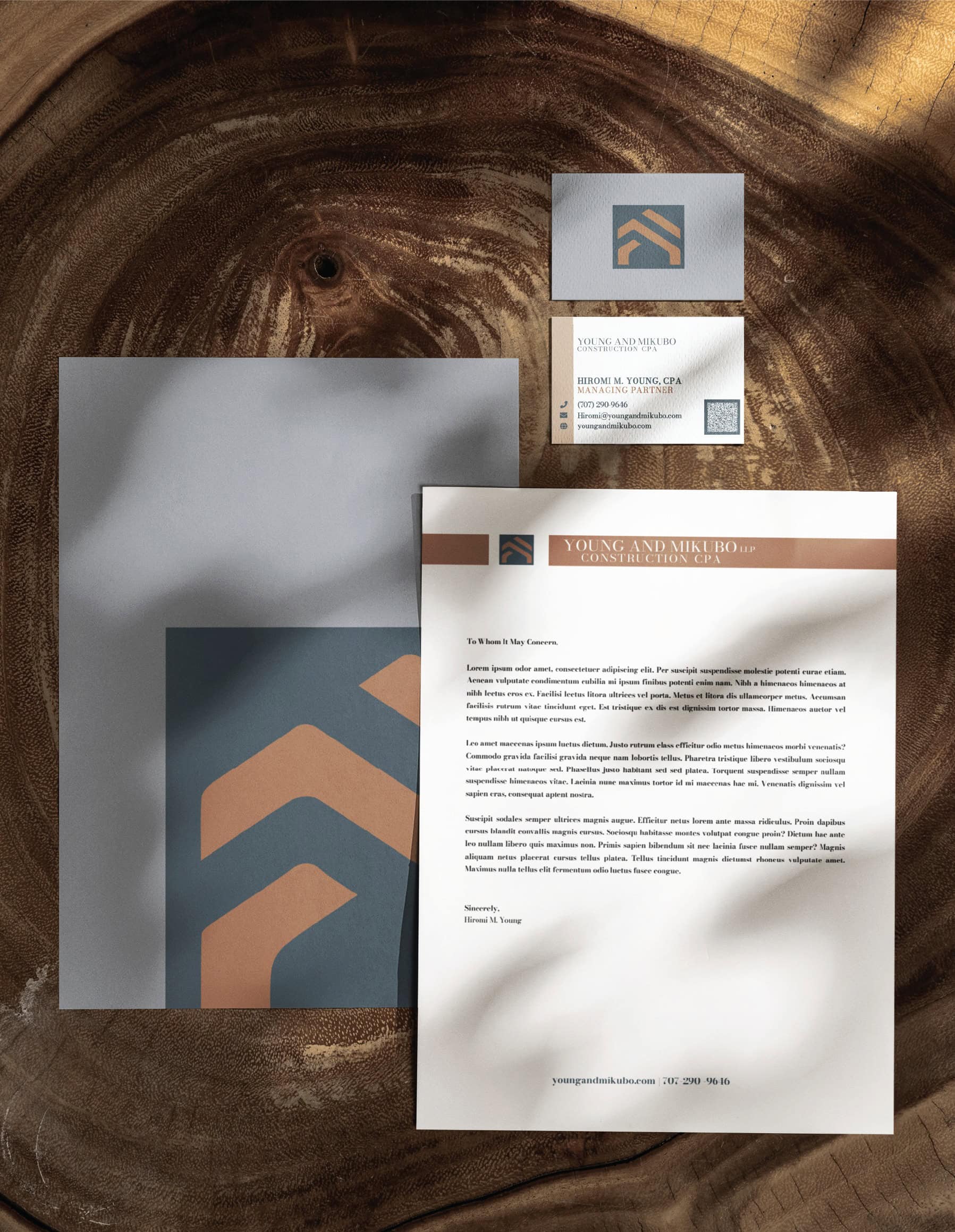Branding kit for Young and Mikubo Construction CPA, including a business card, letterhead, and folder, arranged on a dark wood surface to showcase professional Texas accounting services.